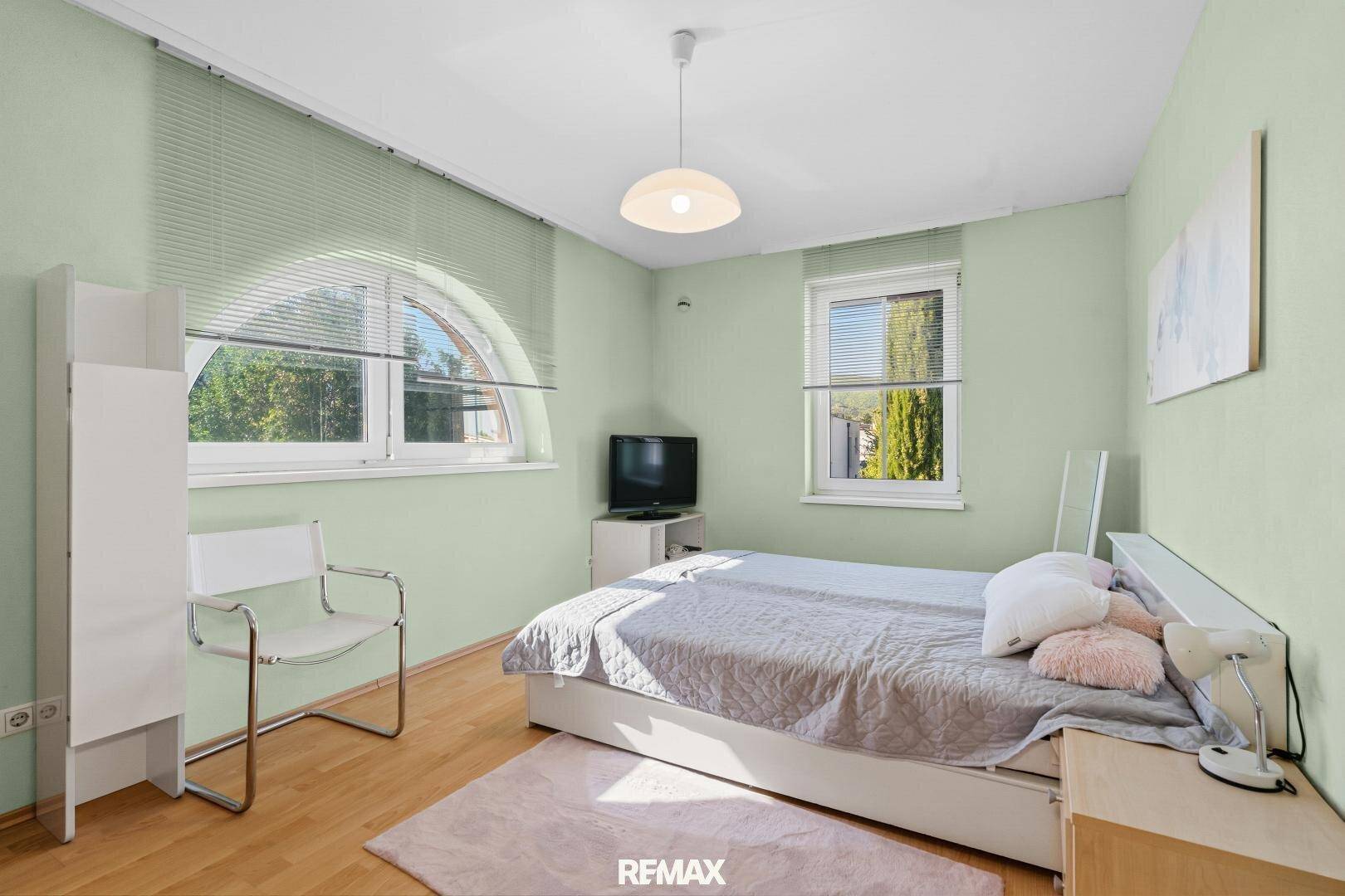 Gemütliches Schlafzimmer mit hellem Holzboden und Fenster mit Blick ins Grüne.