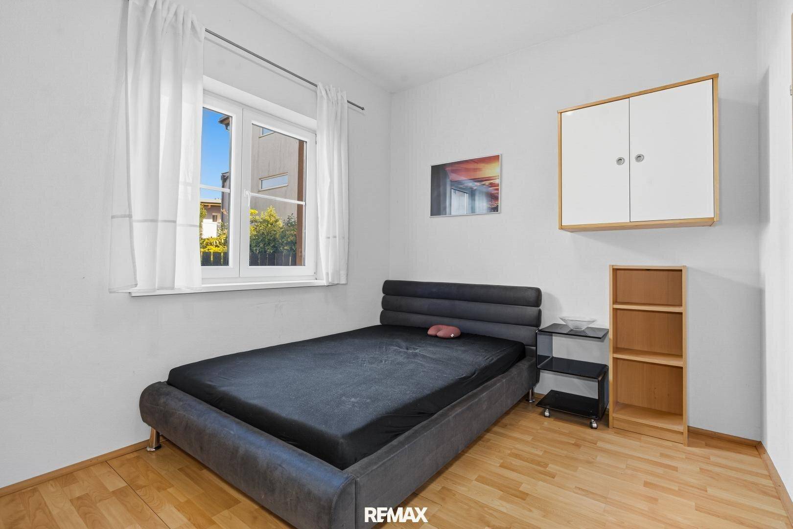 Schlafzimmer mit dunklem Bett, Holzboden und einem Fenster mit Blick nach draußen.
