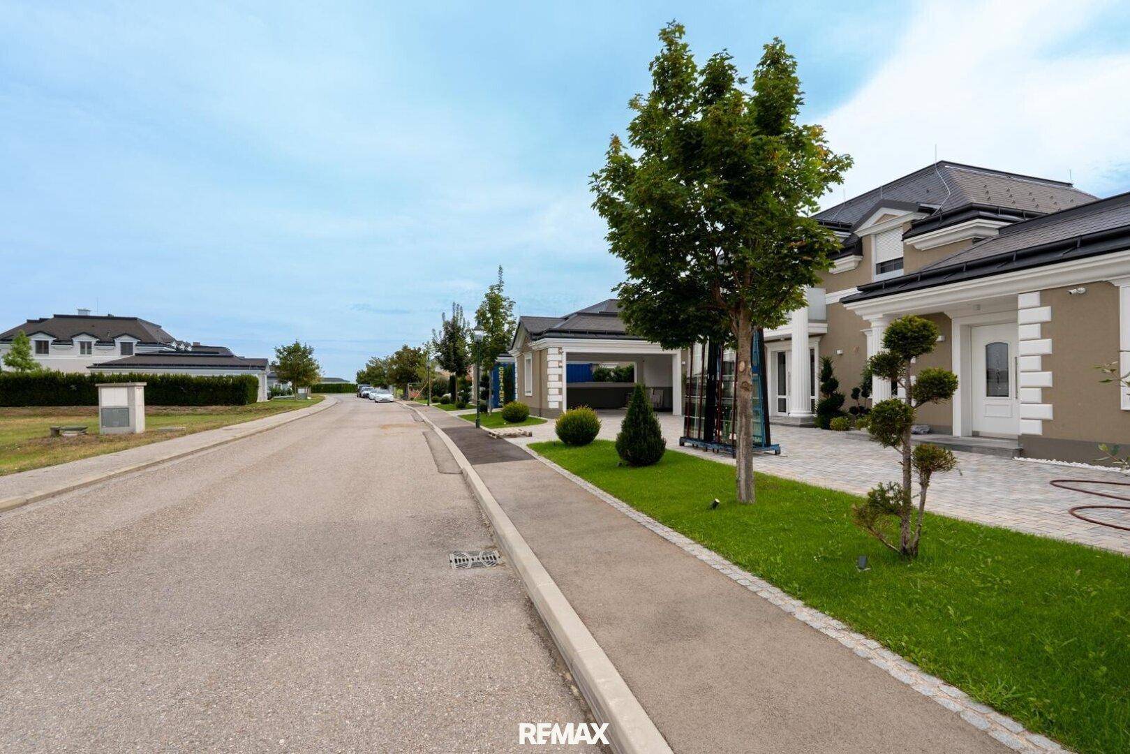 Blick von der Straße auf einen Neubau mit gepflegtem Vorgarten und breitem Bürgersteig.