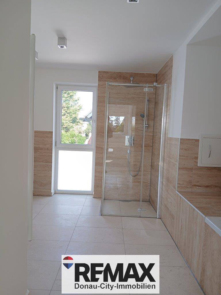 Modernes Badezimmer mit begehbarer Dusche und hellen Fliesen, das viel Tageslicht bietet.