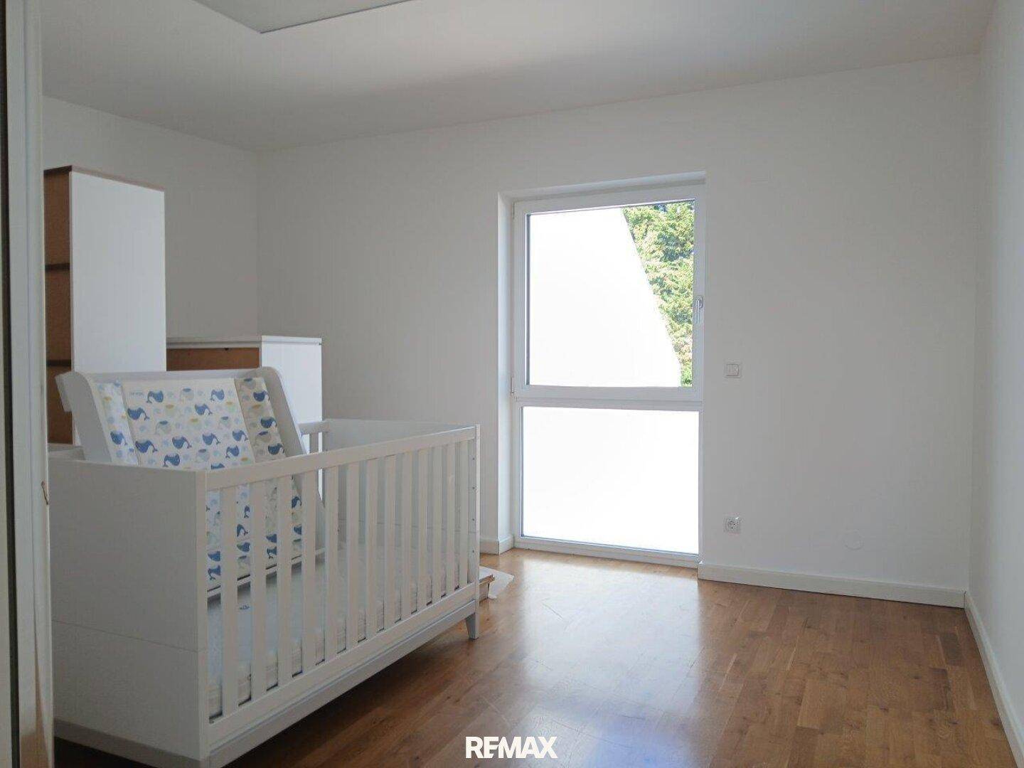Helles Kinderzimmer mit Babybett und schönem Hartholzboden.