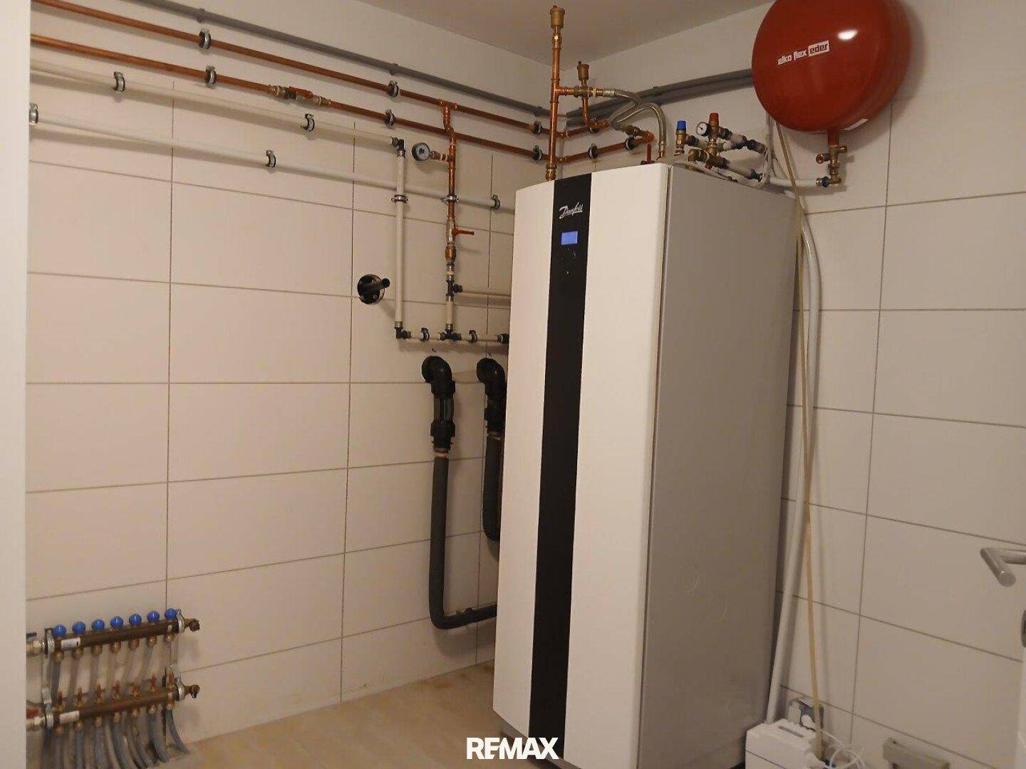 Technikraum mit moderner Wärmepumpe und sichtbaren Installationen an den gefliesten Wänden.