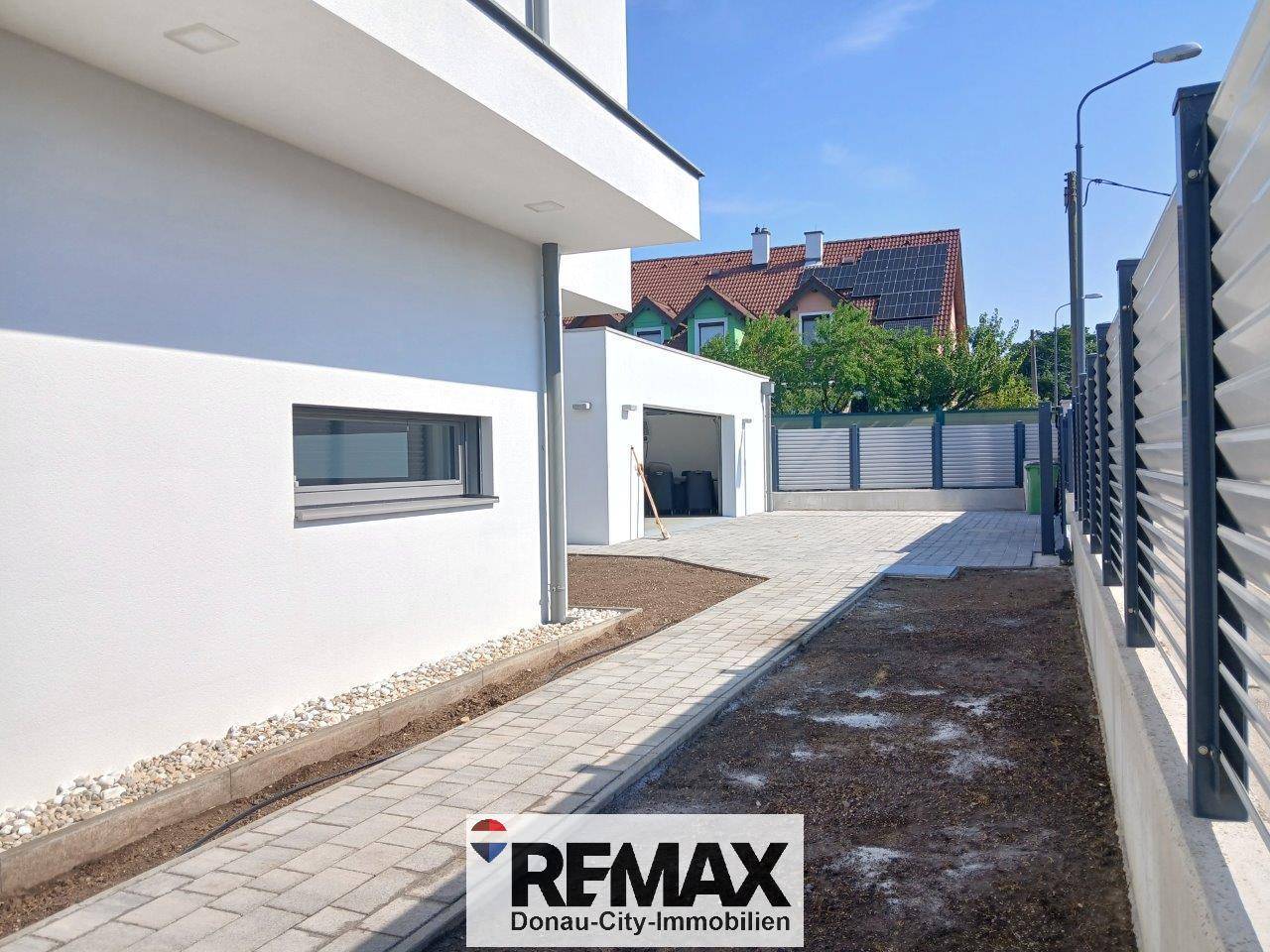 Seitenansicht des modernen Hauses mit gepflasterter Zufahrt und Garage, umgeben von einem Zaun.