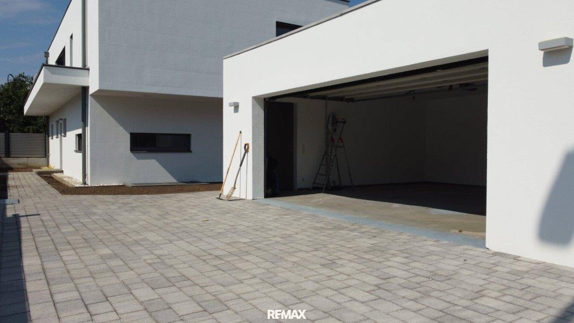 Moderne Doppelgarage mit gepflasterter Zufahrt und der weißen Fassade des Neubaus.