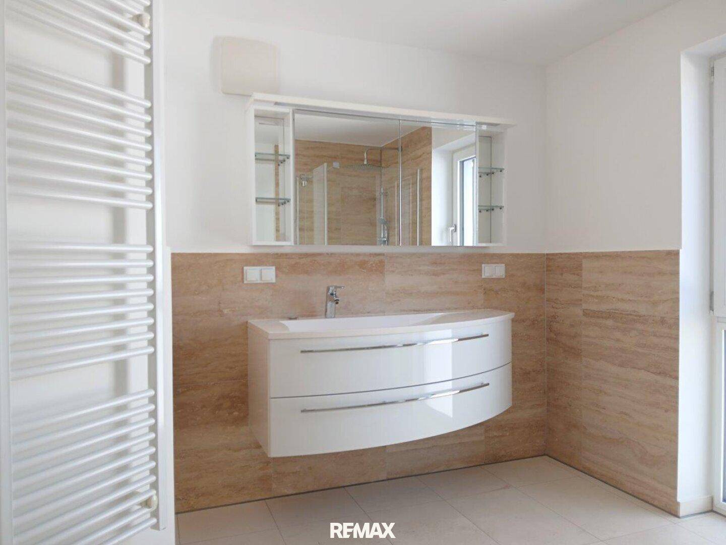 Badezimmer mit modernem Waschtisch, Spiegelschrank und beheiztem Handtuchhalter.