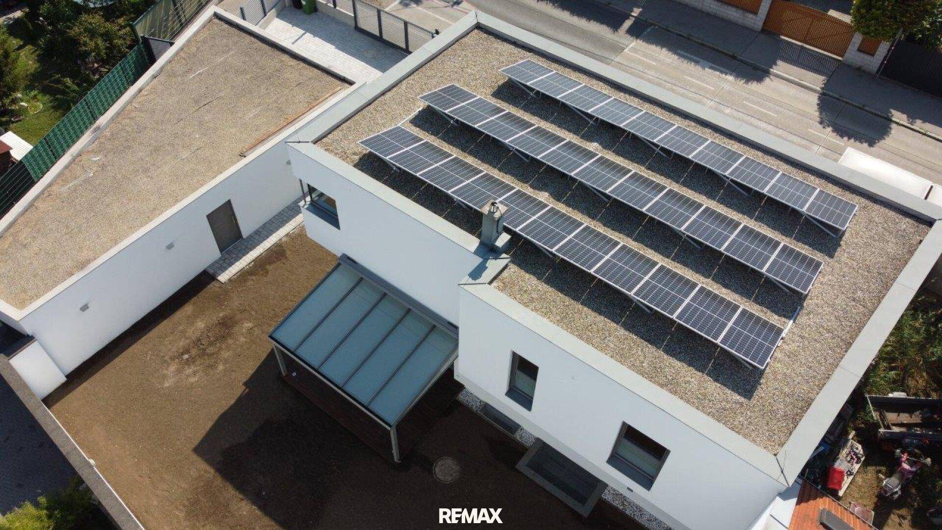 Vogelperspektive eines modernen Hauses mit Flachdach und Photovoltaikanlage auf dem Dach.