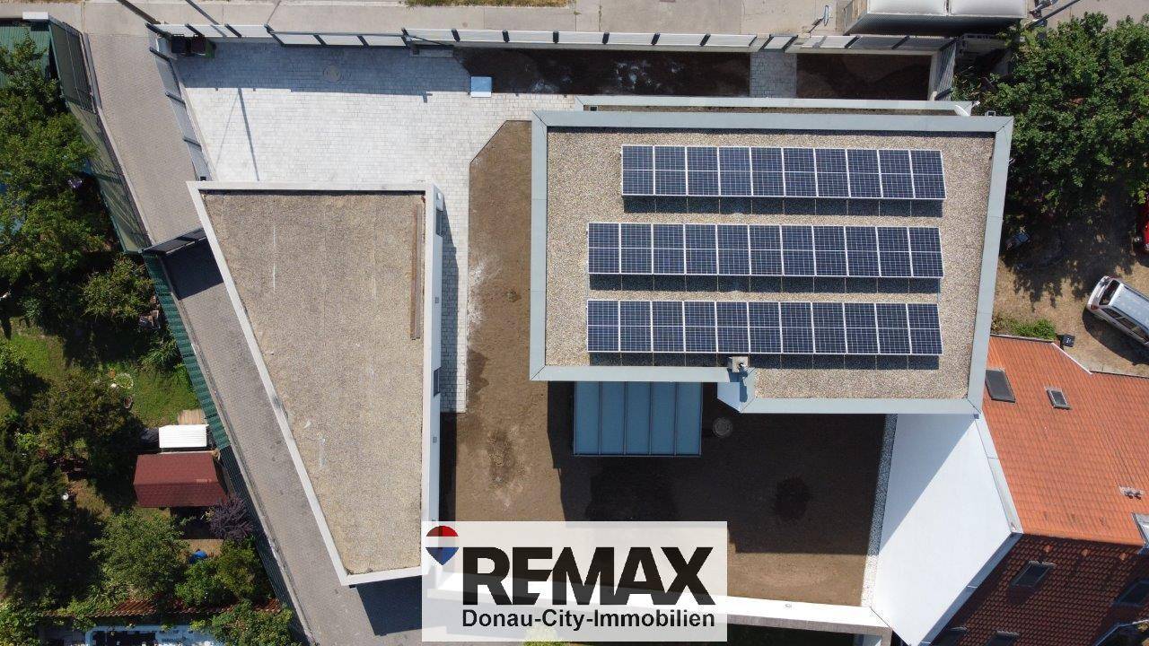 Luftaufnahme eines modernen Hauses mit Flachdach und installierten Photovoltaik-Modulen.