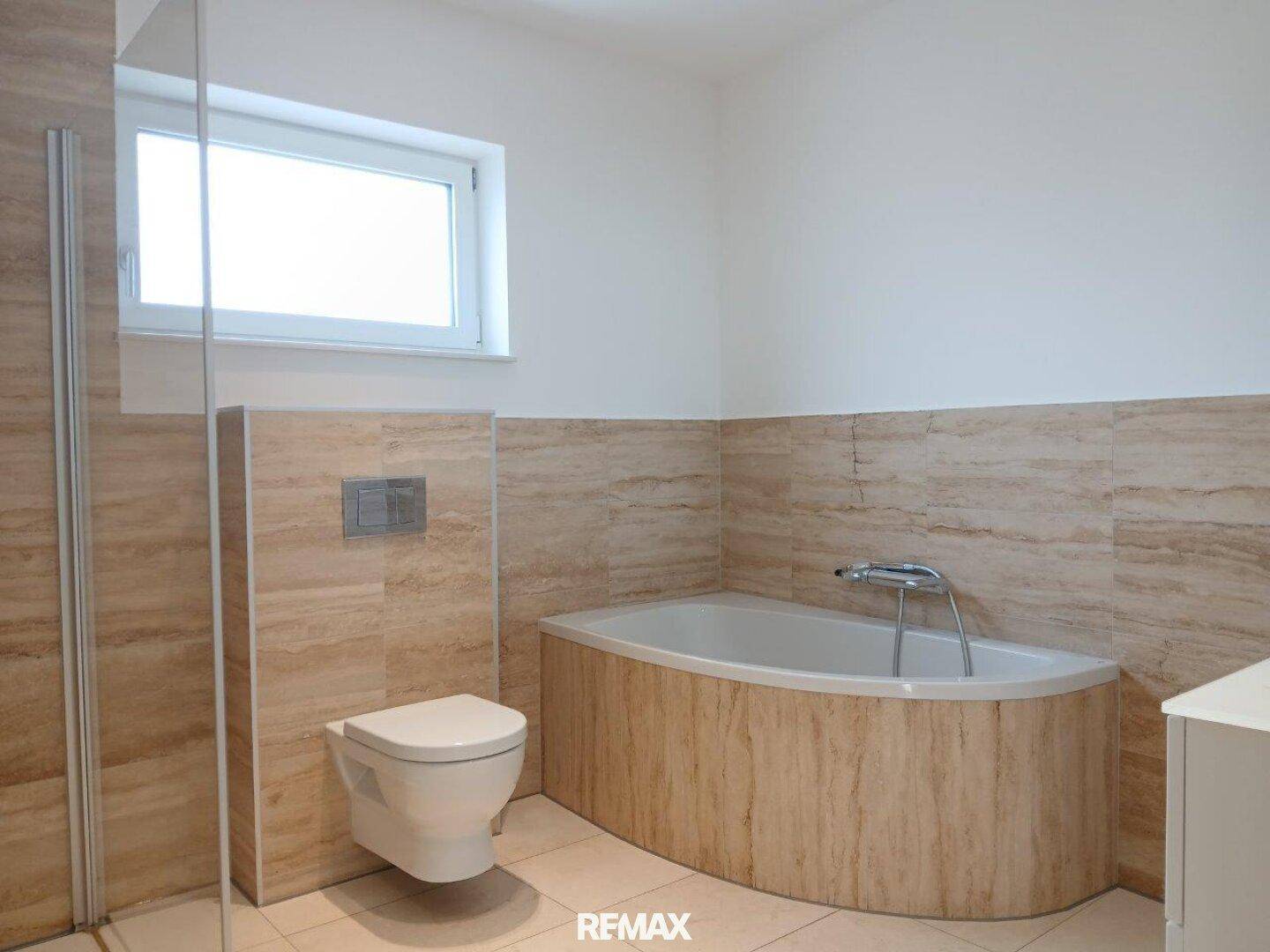 Badezimmer mit wandhängendem WC und einer Eckbadewanne.