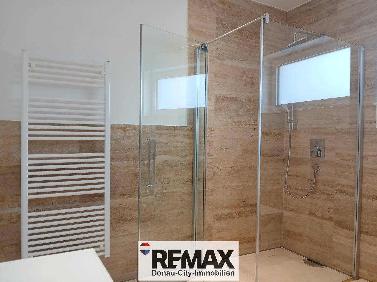 Helles Badezimmer mit großer begehbarer Dusche und praktischem beheiztem Handtuchhalter.