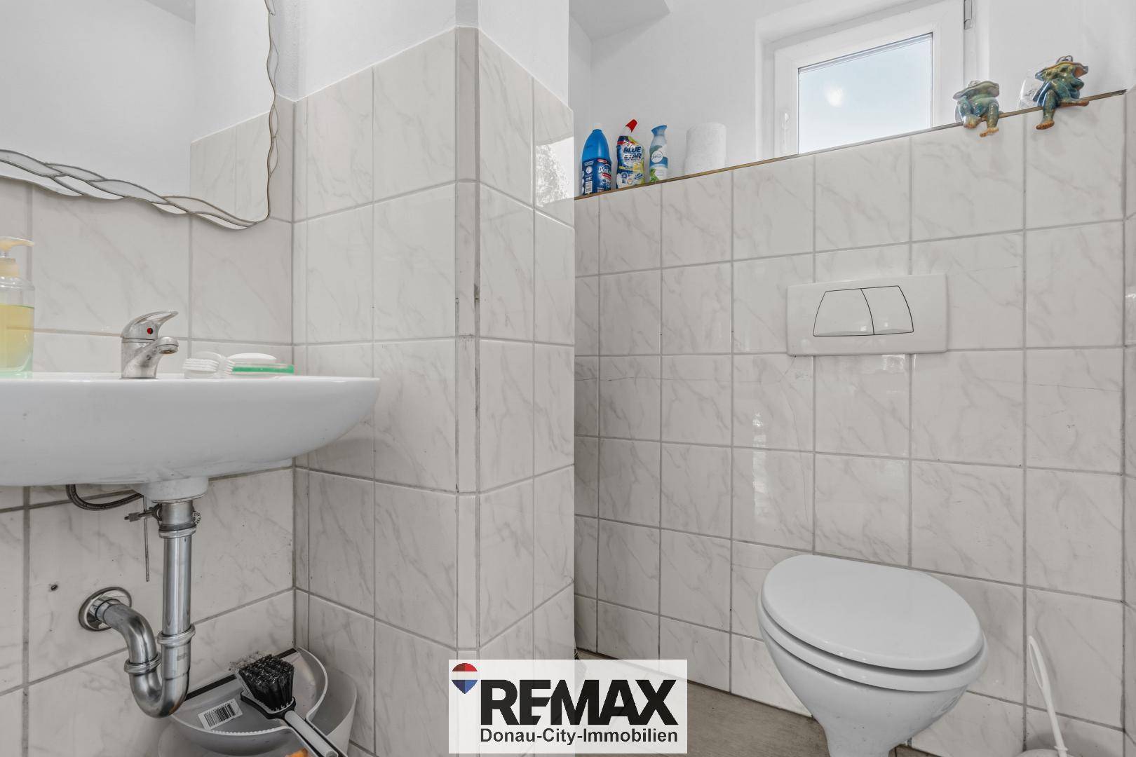 Kleines WC mit weiß gefliesten Wänden, Waschbecken und Fenster.