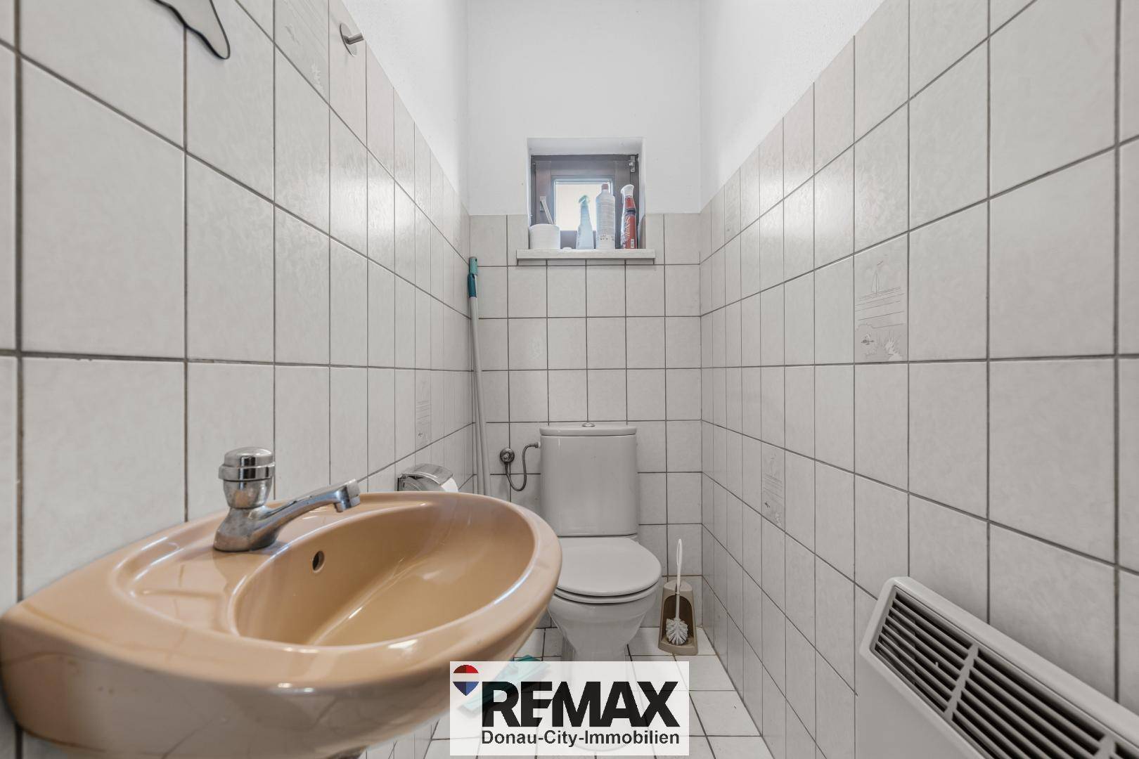 Kleines WC mit Waschbecken, Toilette und Fenster, komplett gefliest.