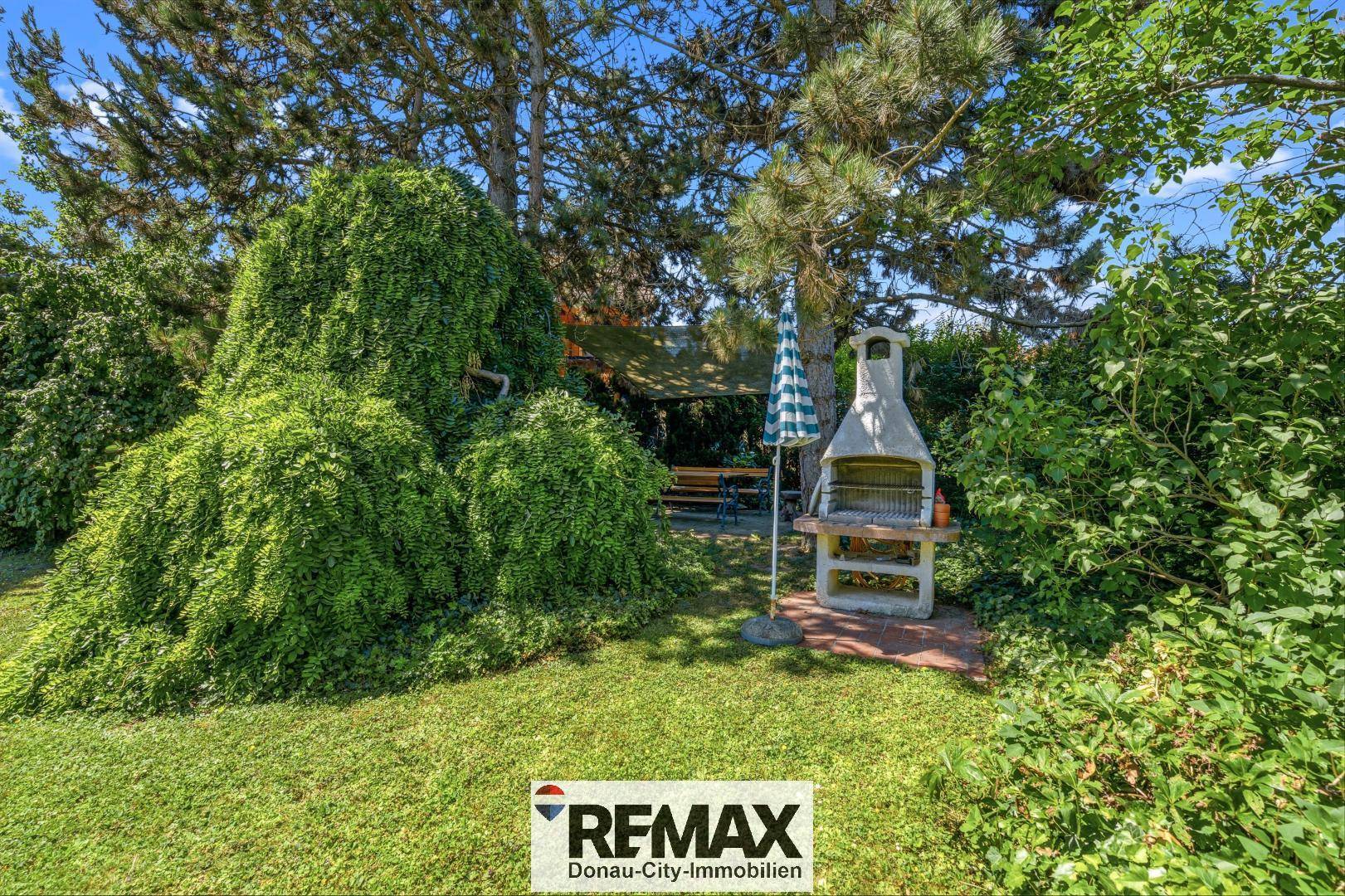 Großer Garten mit Rasenfläche, Bäumen und gemauertem Grillplatz.
