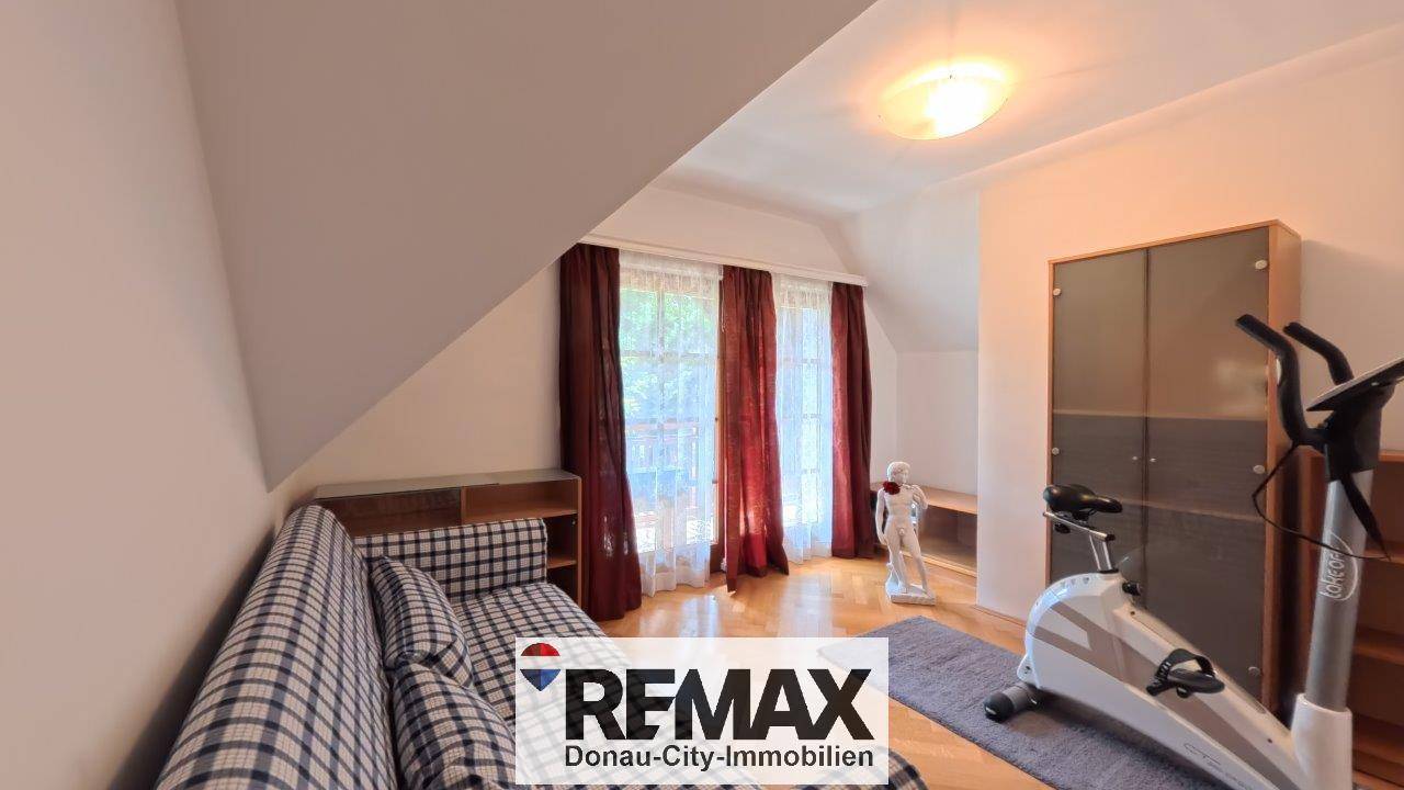 Dachgeschosszimmer mit Fitnessgerät, Sofa und Holzboden, ideal für Sport und Entspannung.