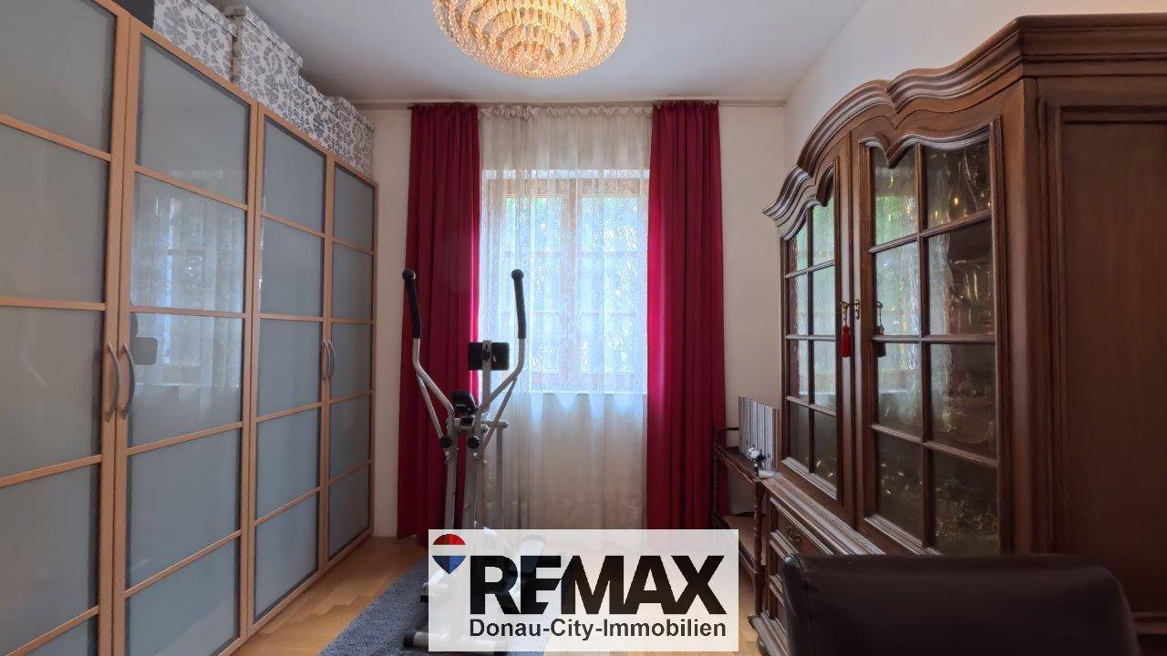 Schlafzimmer mit Einbauschränken, Fitnessgerät und roten Vorhängen, die für Farbakzente sorgen.