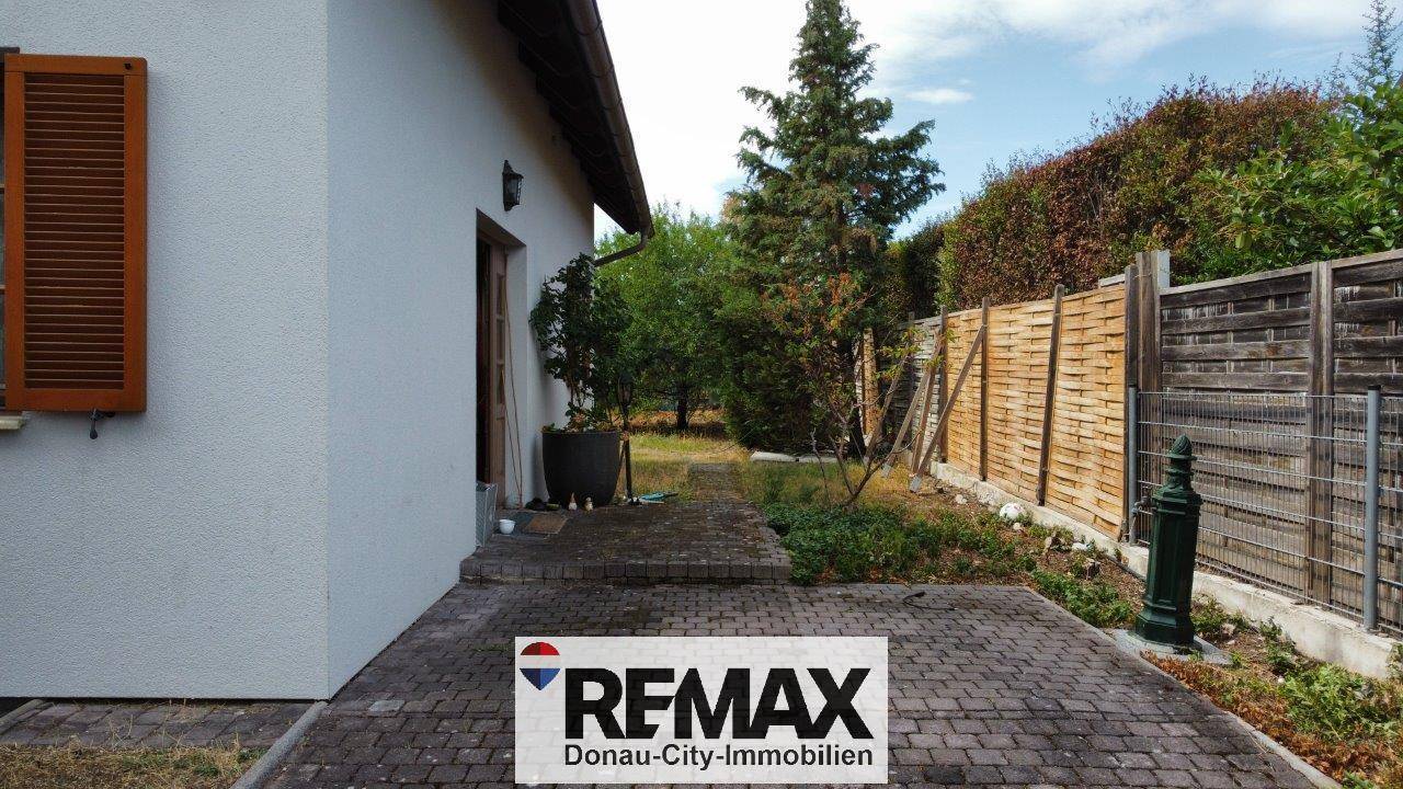 Gepflasterter Bereich neben dem Haus, der in den Garten mit Holzzaun übergeht.