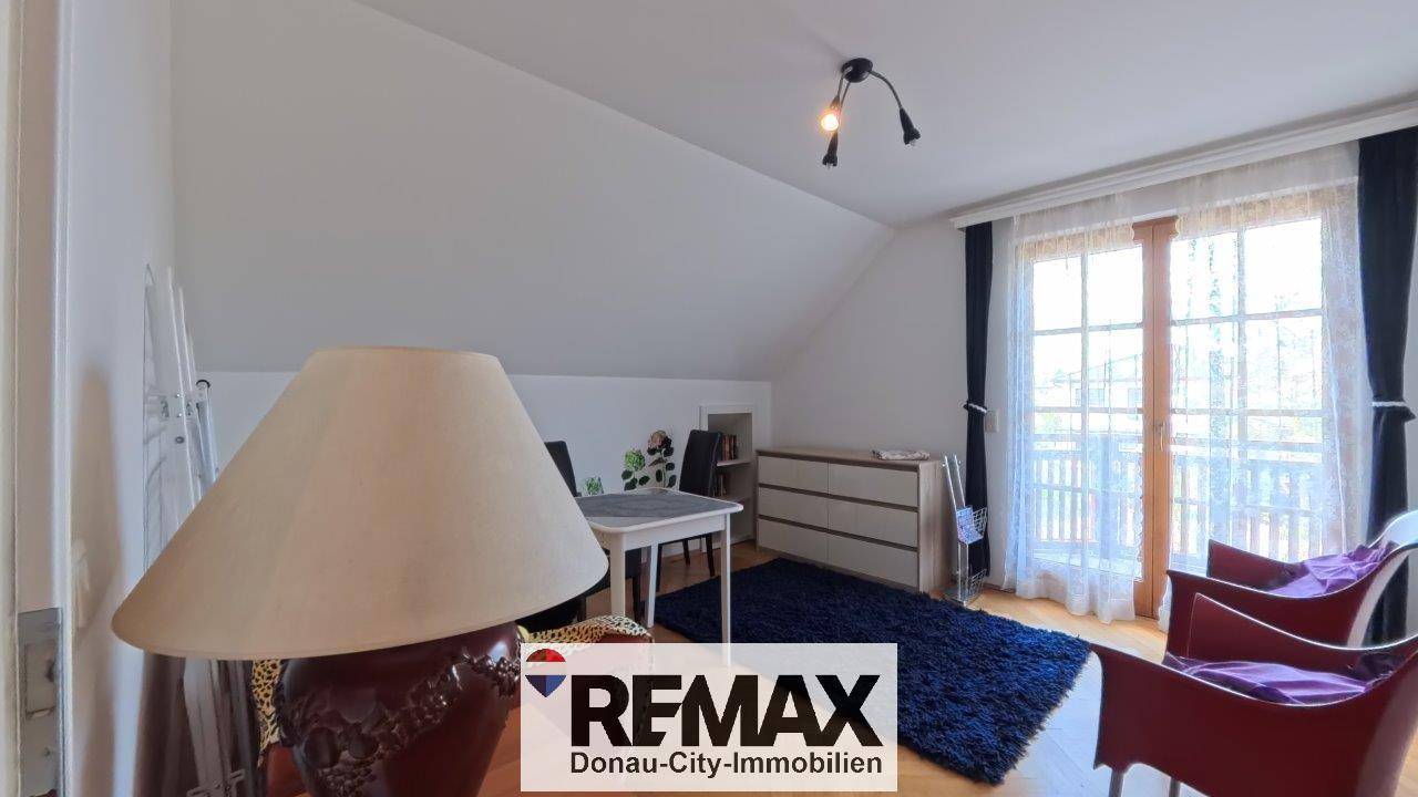 Dachgeschosszimmer mit Teppichboden, Kommode und Zugang zum Balkon, der einen schönen Ausblick ermöglicht.