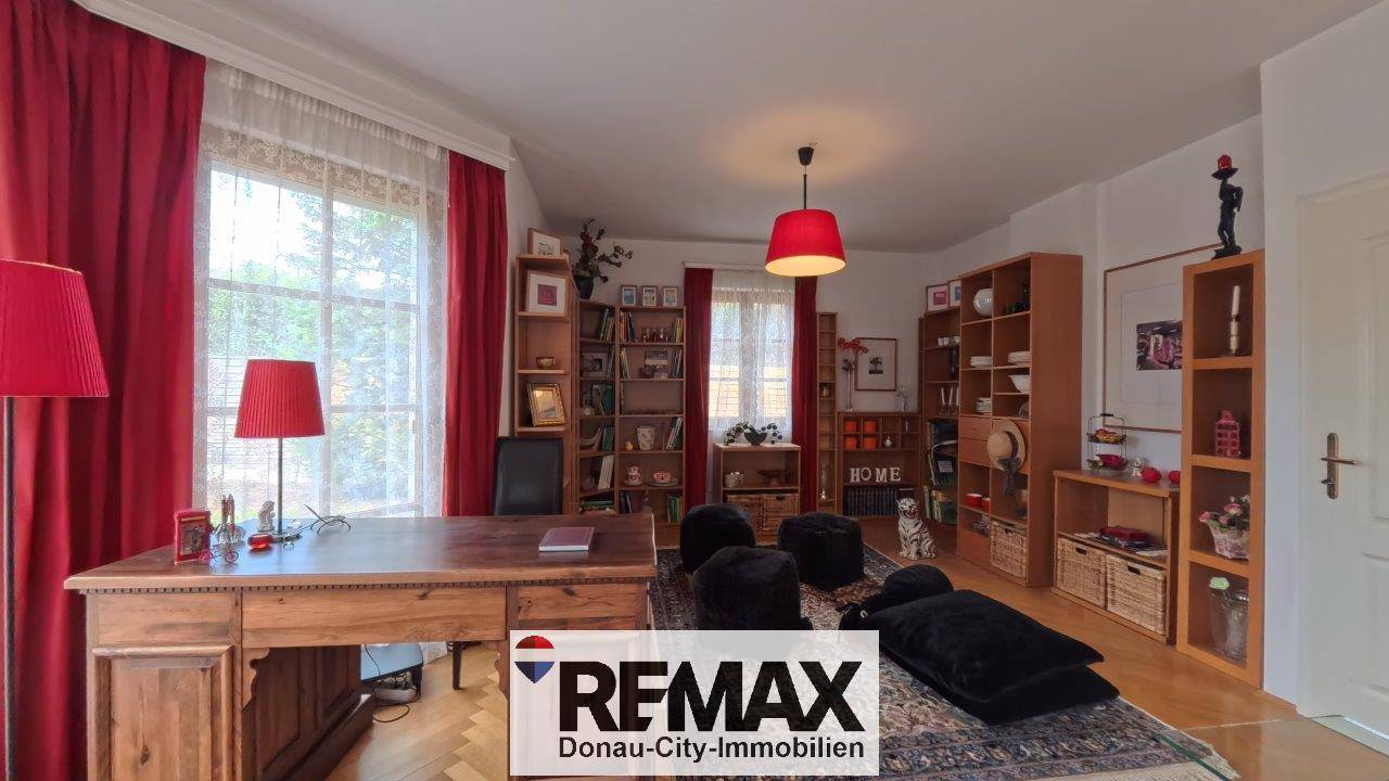 Geräumiges Arbeitszimmer mit Holzschreibtisch, Bücherregalen und roten Akzenten, die eine lebendige Atmosphäre schaffen.