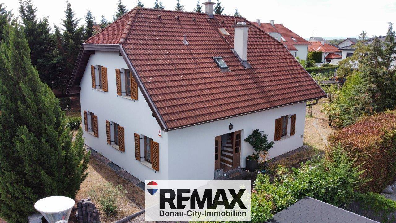 Luftaufnahme des Einfamilienhauses mit weißer Fassade, rotem Ziegeldach und grüner Umgebung.