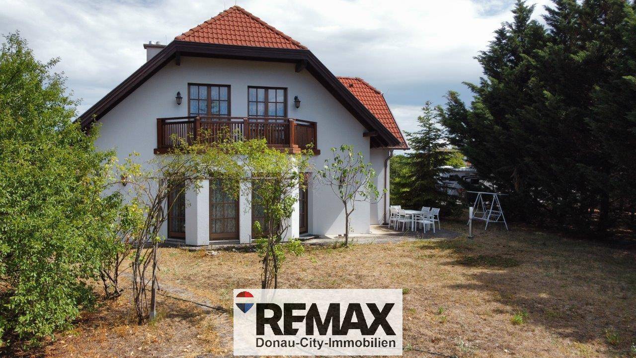 Rückseite des Hauses mit Terrasse, Schaukel und großem Gartenbereich mit Rasen.