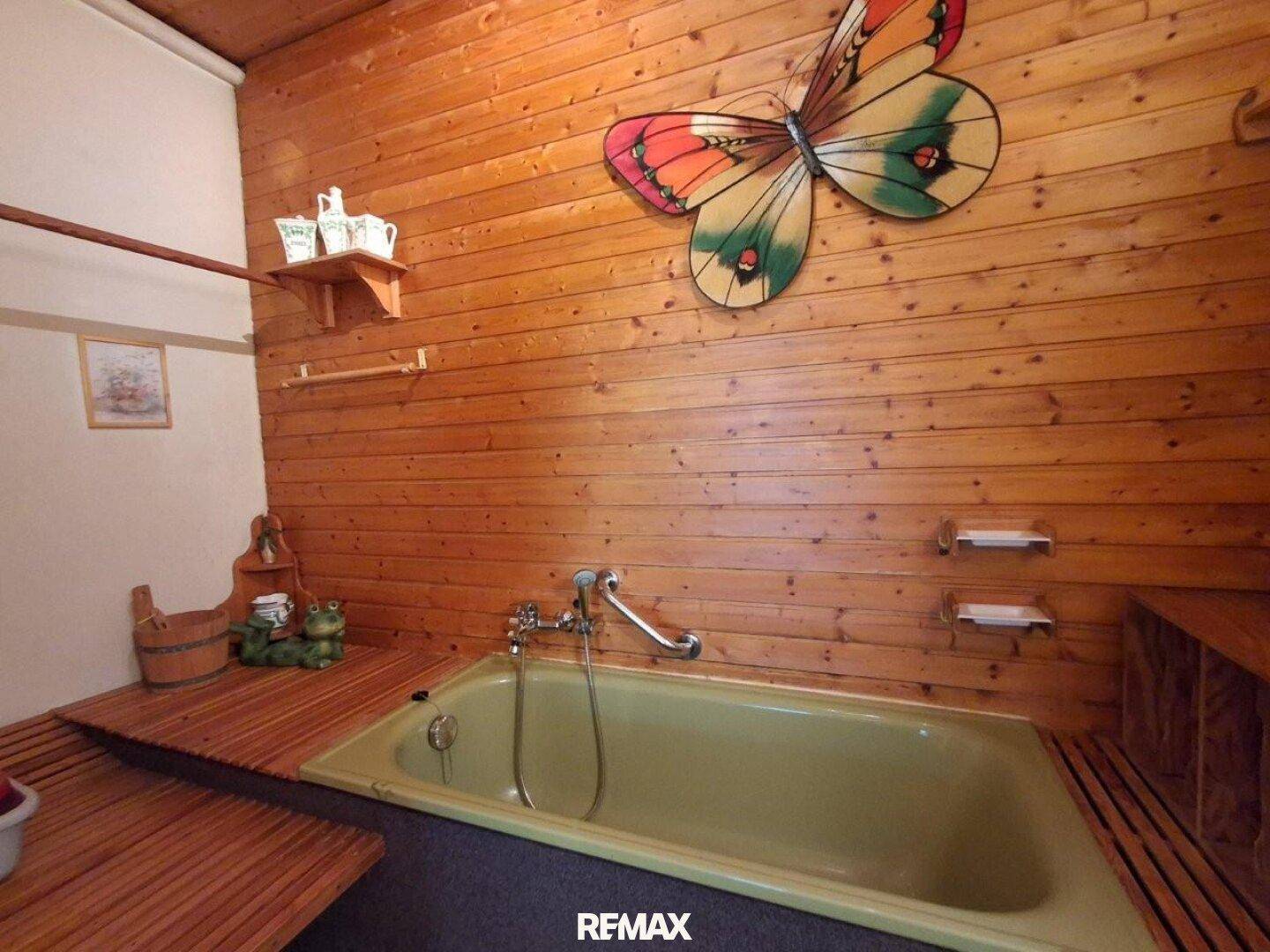 Detailansicht der grünen Badewanne in einem rustikalen Badezimmer mit Holztäfelung und Ablageflächen.