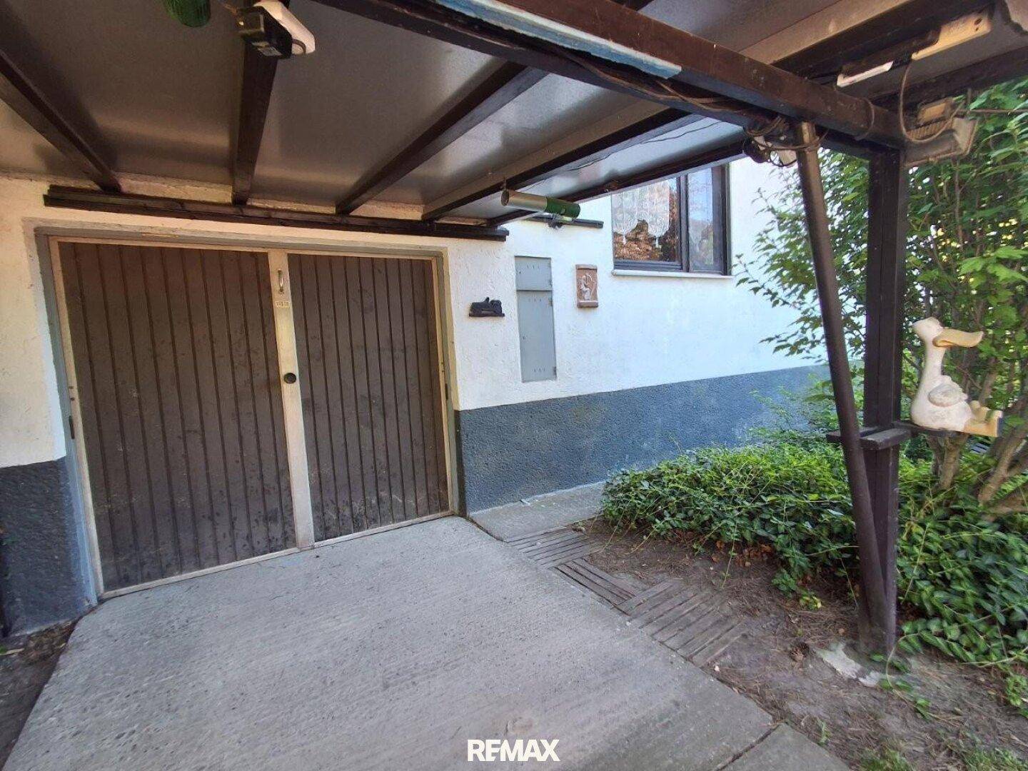 Überdachter Eingangsbereich zur Garage oder zum Carport mit Holztüren und Betonboden.