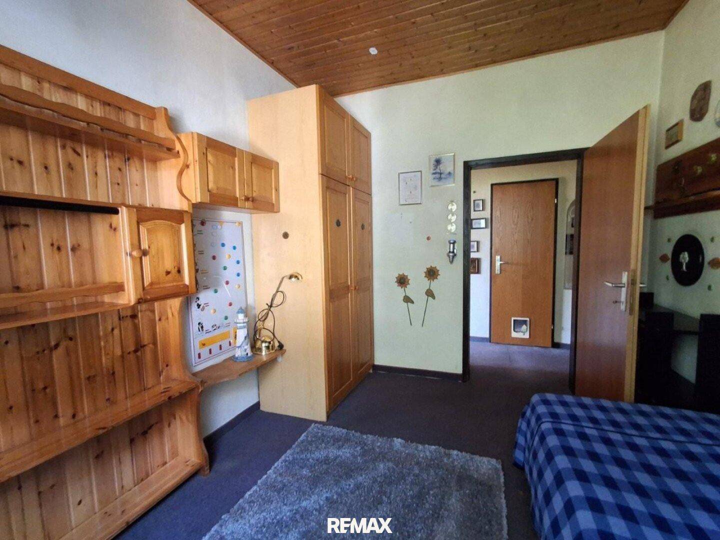 Schlafzimmer mit Bett, Holzmöbeln und Zugang zum Flur, einfach und funktional eingerichtet.