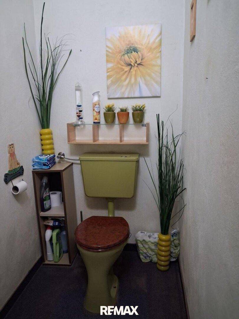 Kleines Gäste-WC mit gelber Toilette, einfacher Einrichtung und dekorativen Pflanzen.