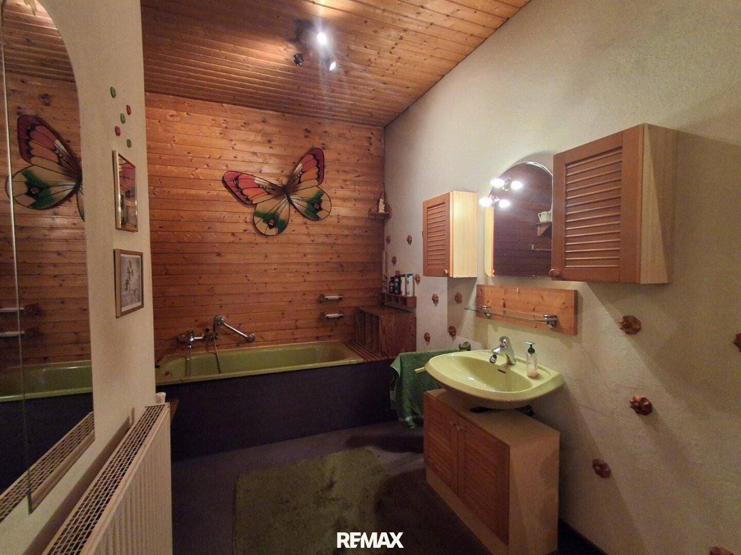 Rustikales Badezimmer mit Holztäfelung, grüner Badewanne und Waschbecken, dekoriert mit einem Schmetterling.