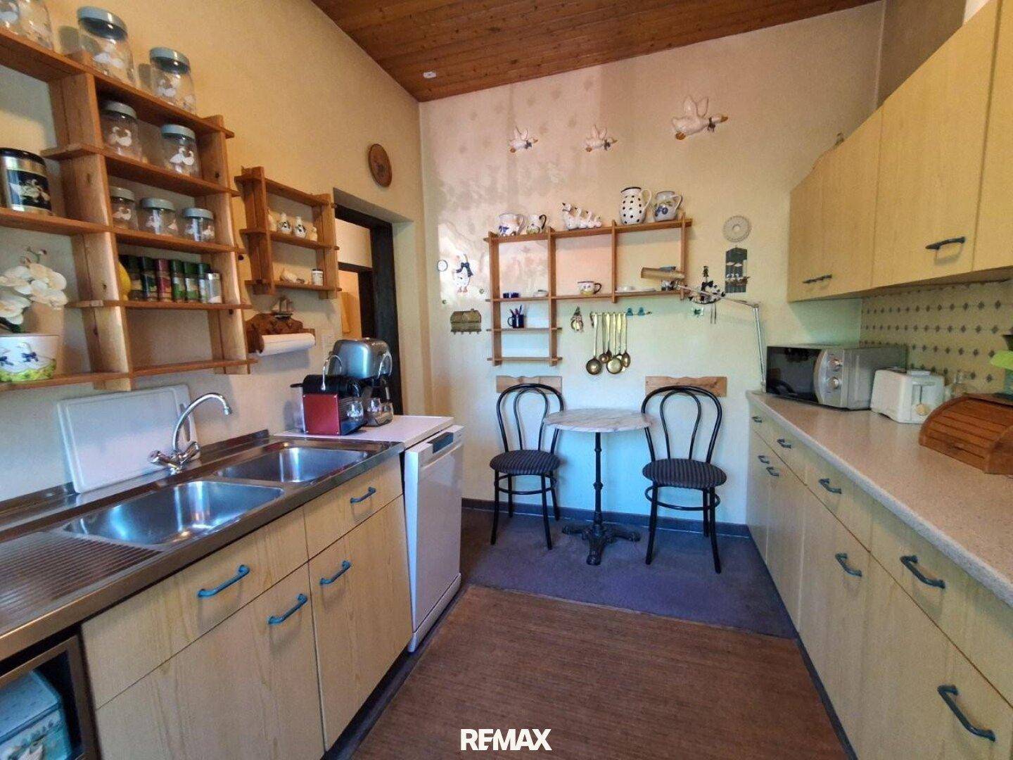Funktionale Küche im Landhausstil mit hellen Holzschränken, Doppelspüle und kleinem Esstisch.