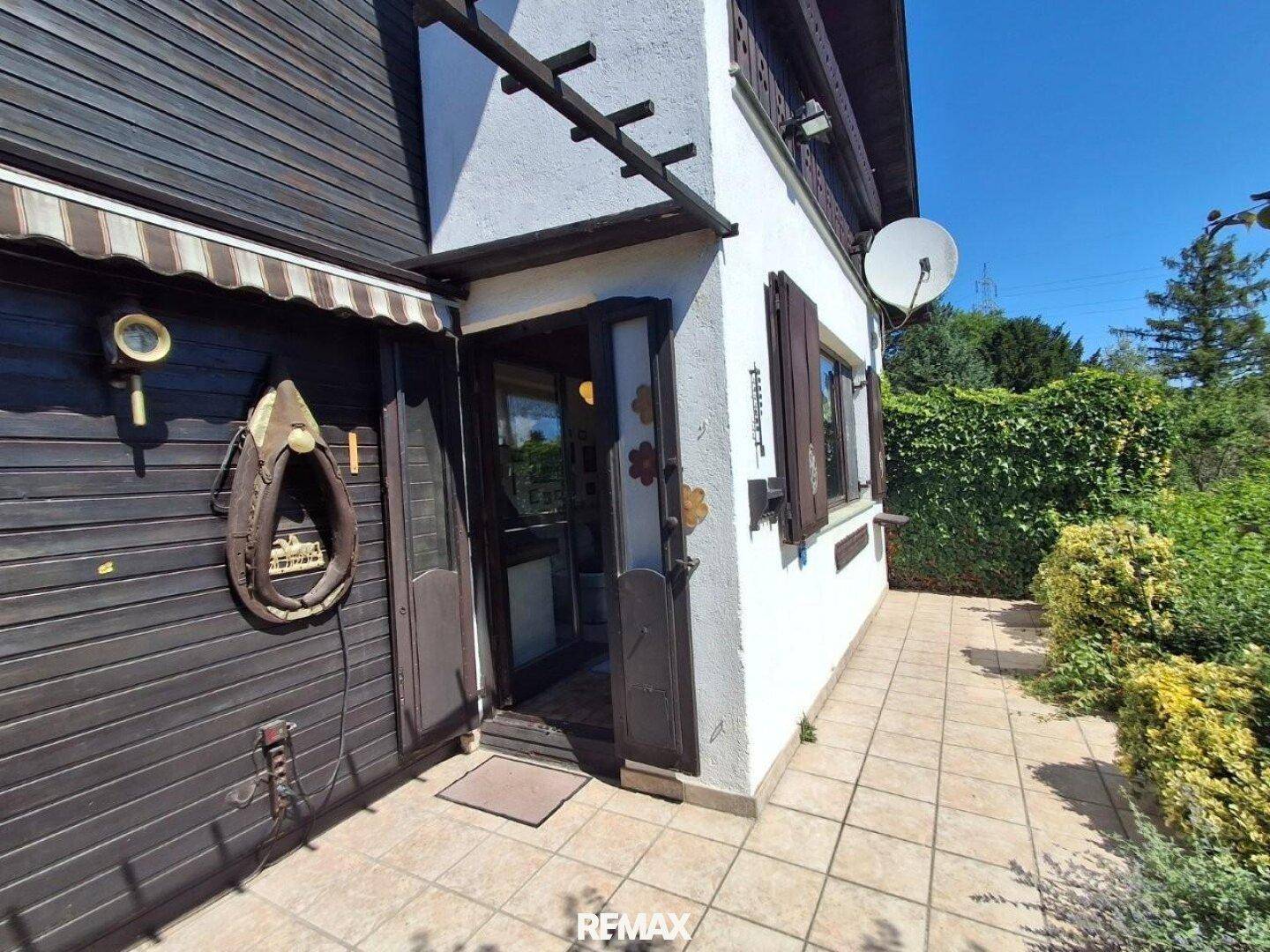 Seitlicher Eingangsbereich des Hauses mit gefliestem Weg, Holzakzenten und einer Hecke.