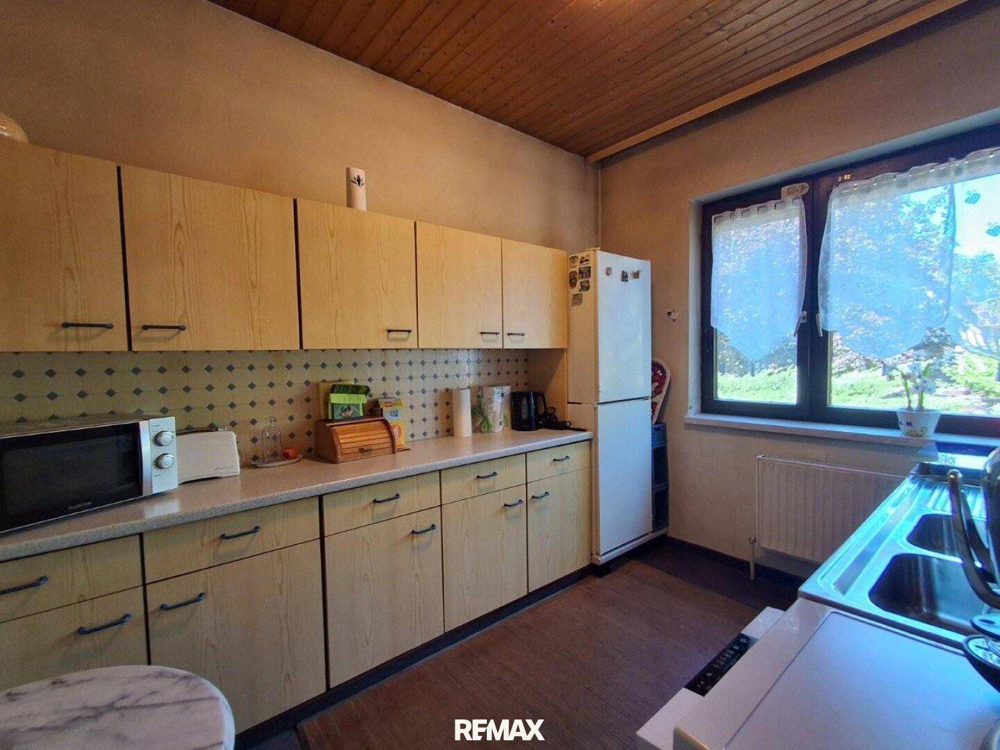 Helle Küche mit Holzschränken, Kühlschrank und Mikrowelle, bietet einen Blick in den Garten.