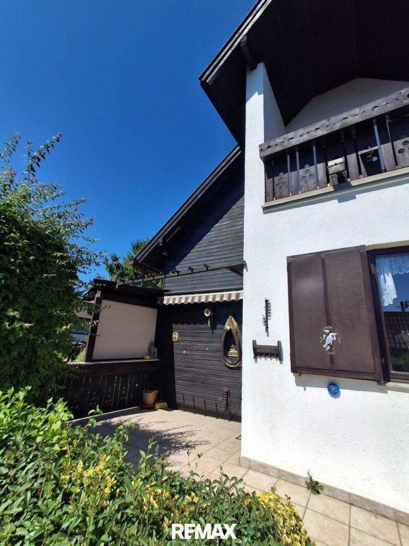 Seitenansicht des Hauses mit Holzelementen, Fensterläden und einem kleinen Vordach über dem Eingang.