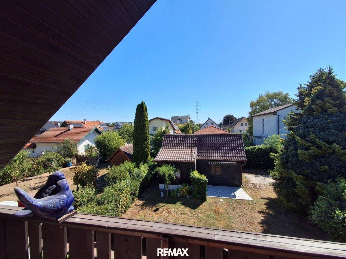 Blick vom Balkon auf den Garten und die umliegenden Häuser mit viel Grün und blauem Himmel.