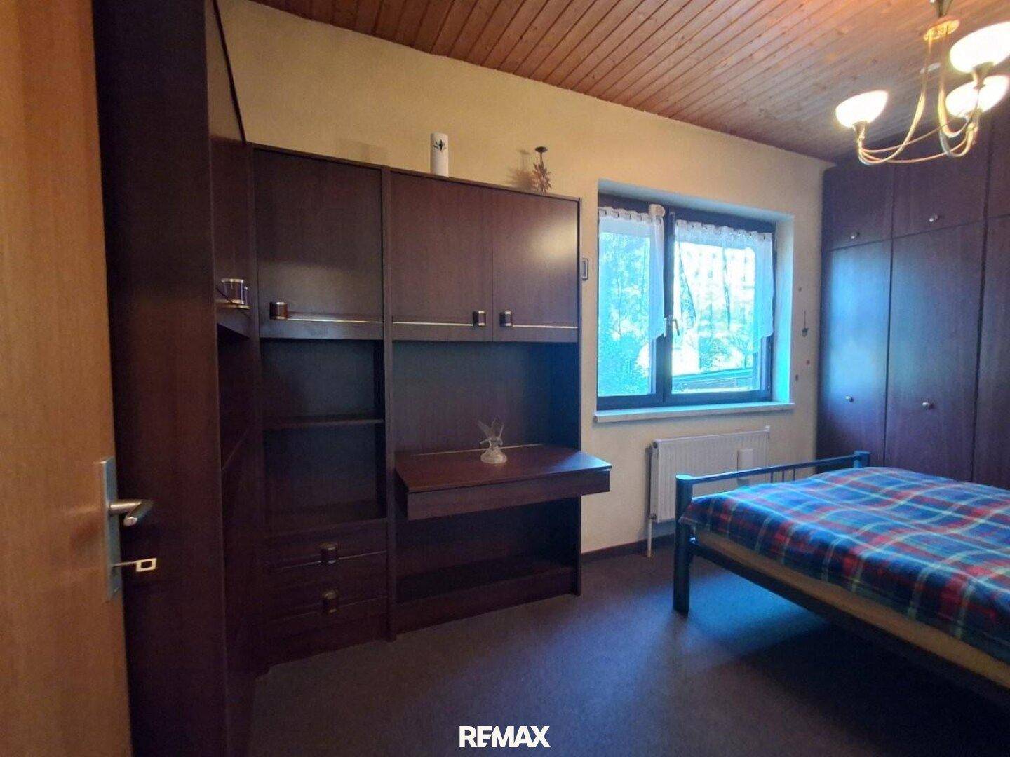 Schlafzimmer mit Bett, Schrankwand und Fenster, das viel Tageslicht hereinlässt, funktional eingerichtet.