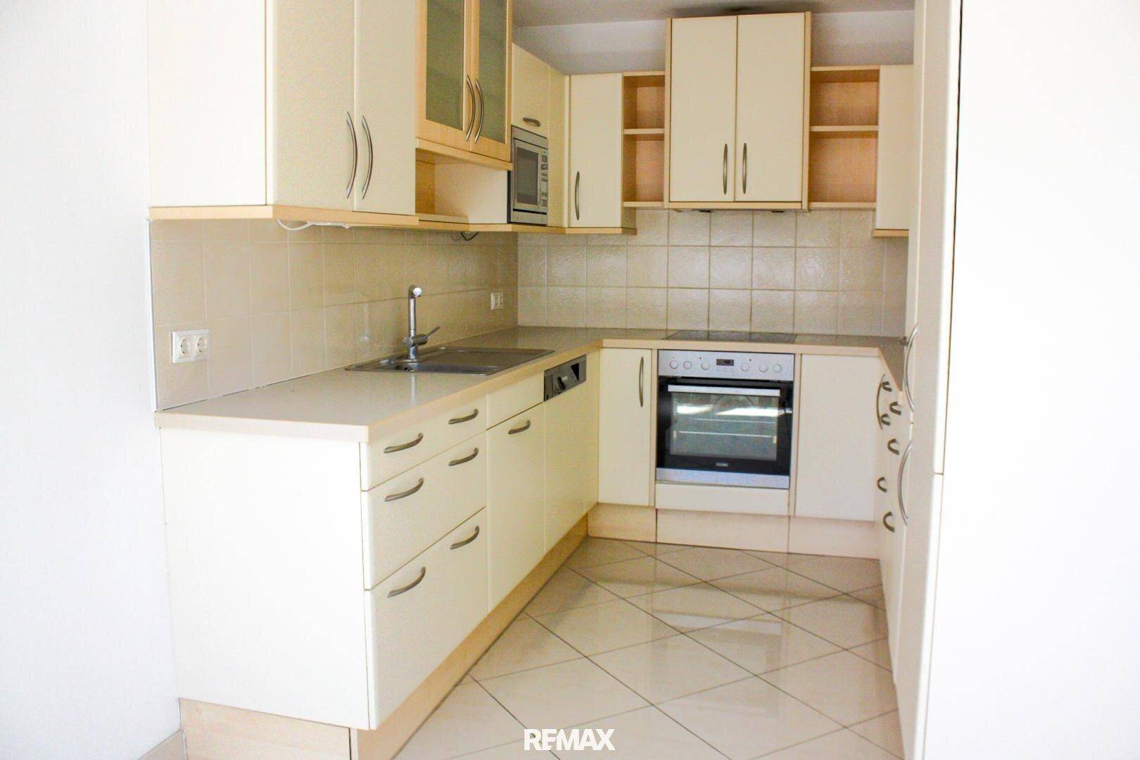 Funktionale Einbauküche in hellem Beige mit integrierten Geräten und Fliesenboden.