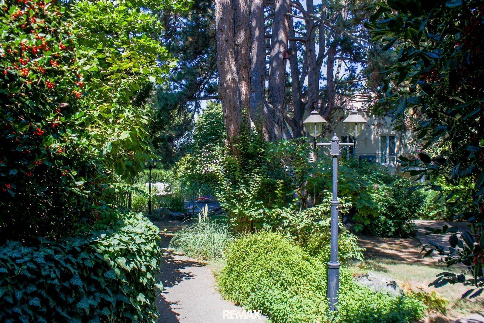 Idyllischer Gartenweg umgeben von üppigem Grün und hohen Bäumen, mit klassischer Gartenbeleuchtung.