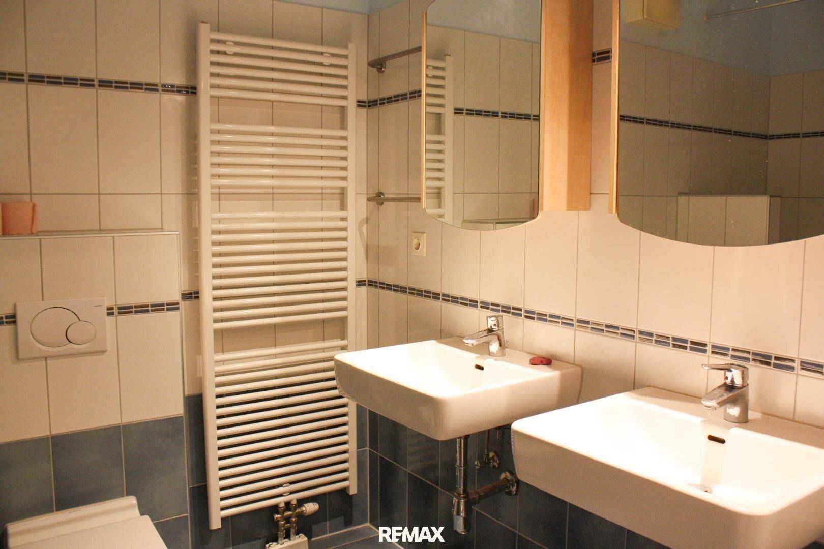 Modernes Badezimmer mit blauen und weißen Fliesen, Doppelwaschbecken und beheiztem Handtuchhalter.