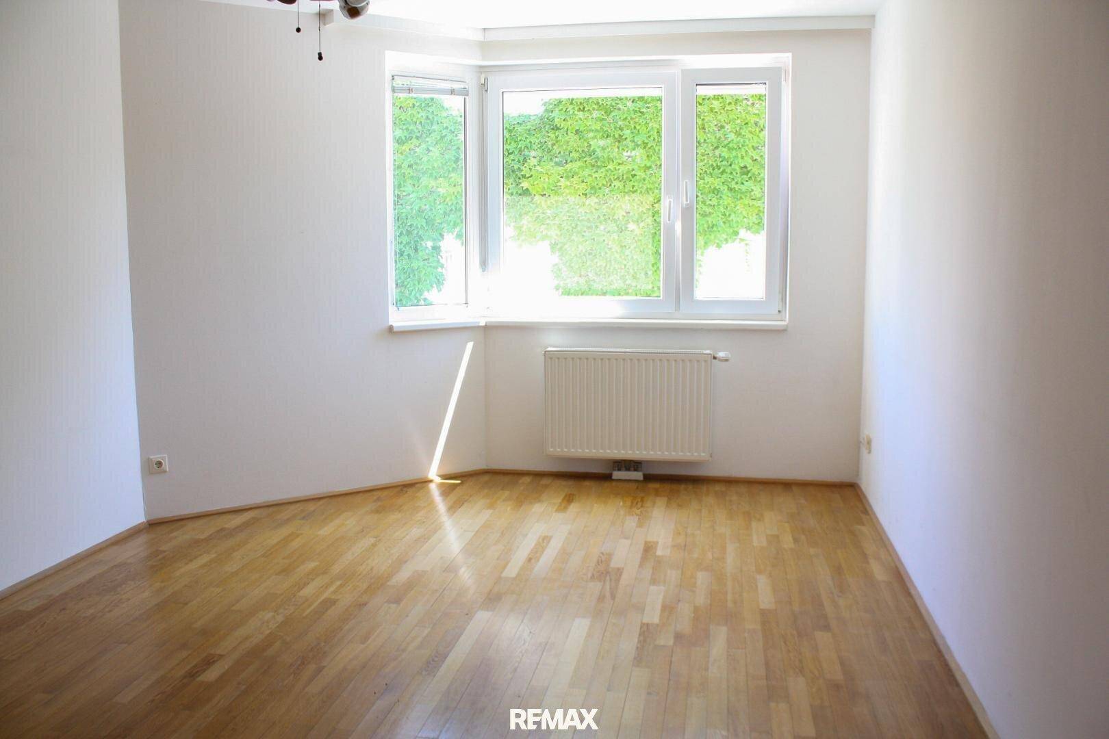 Heller Wohnraum mit Parkettboden und Erkerfenster, das einen Blick ins Grüne bietet.