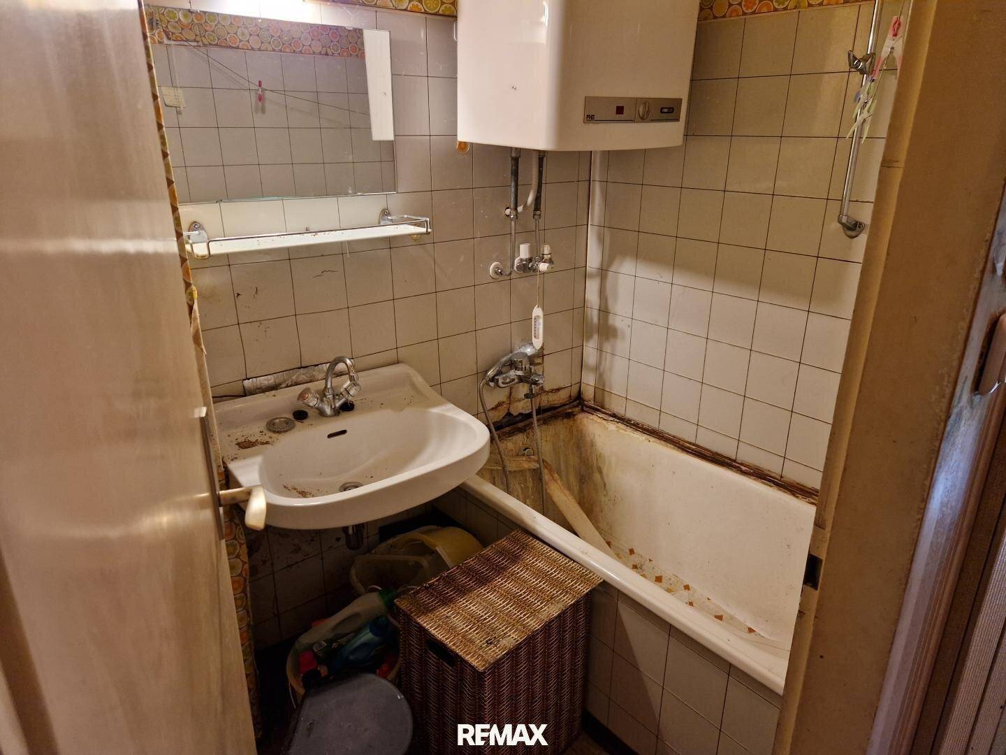 Badezimmer im Originalzustand mit Badewanne, Waschbecken und weißen Fliesen.