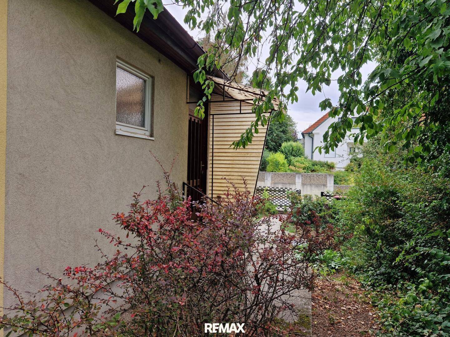 Seitenansicht des Hauses mit einem kleinen Vordach und üppiger Bepflanzung.