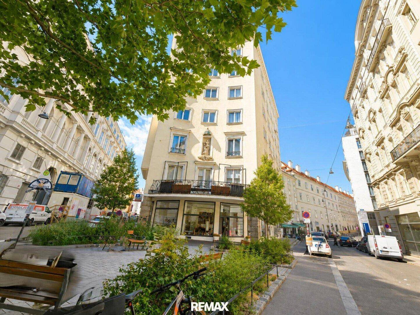 Mehrstöckiges Gebäude an einer Straßenecke mit Bäumen und städtischer Umgebung.