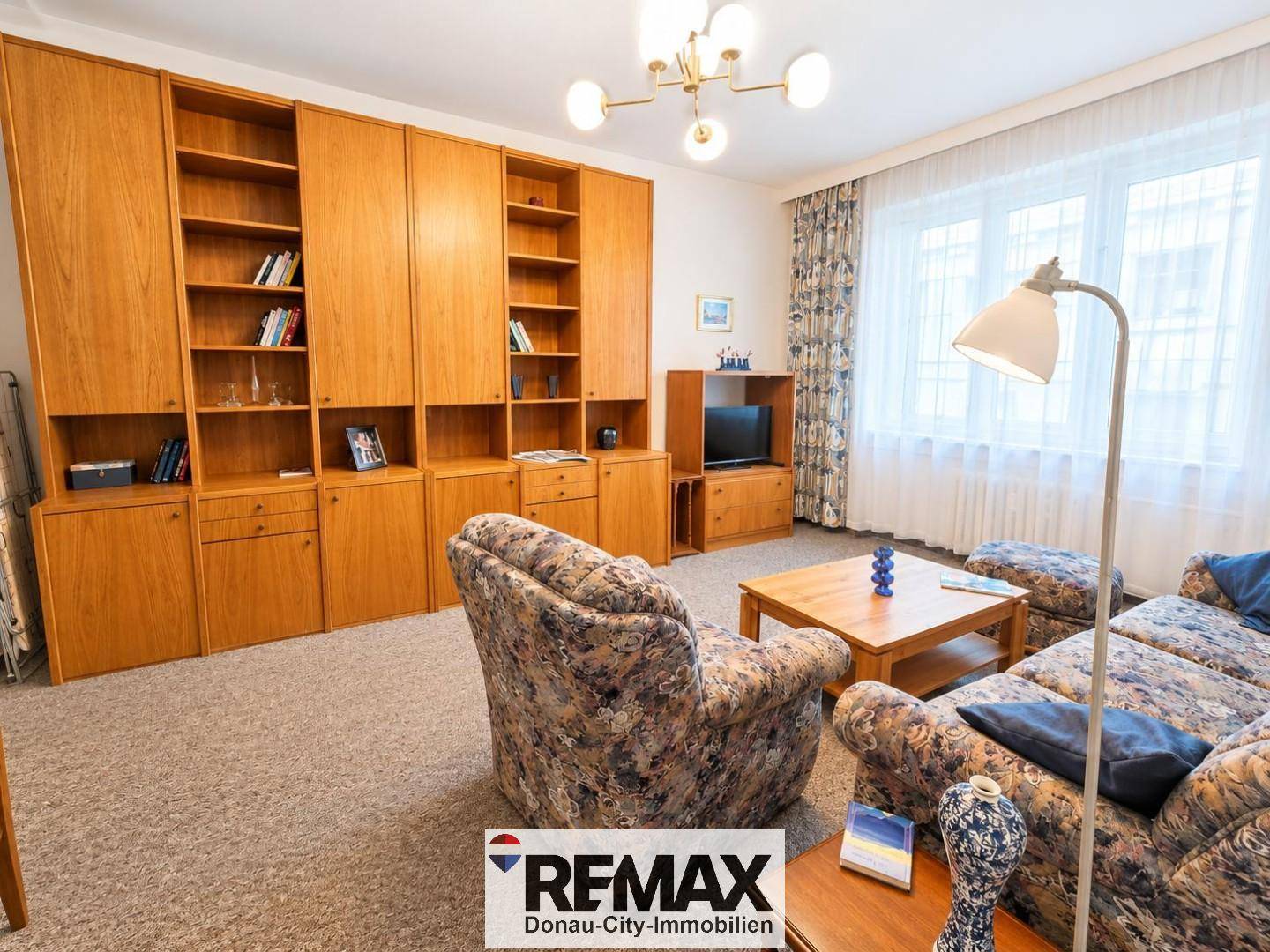 Geräumiges Wohnzimmer mit Teppichboden, großer Schrankwand und bequemen Sitzmöbeln.
