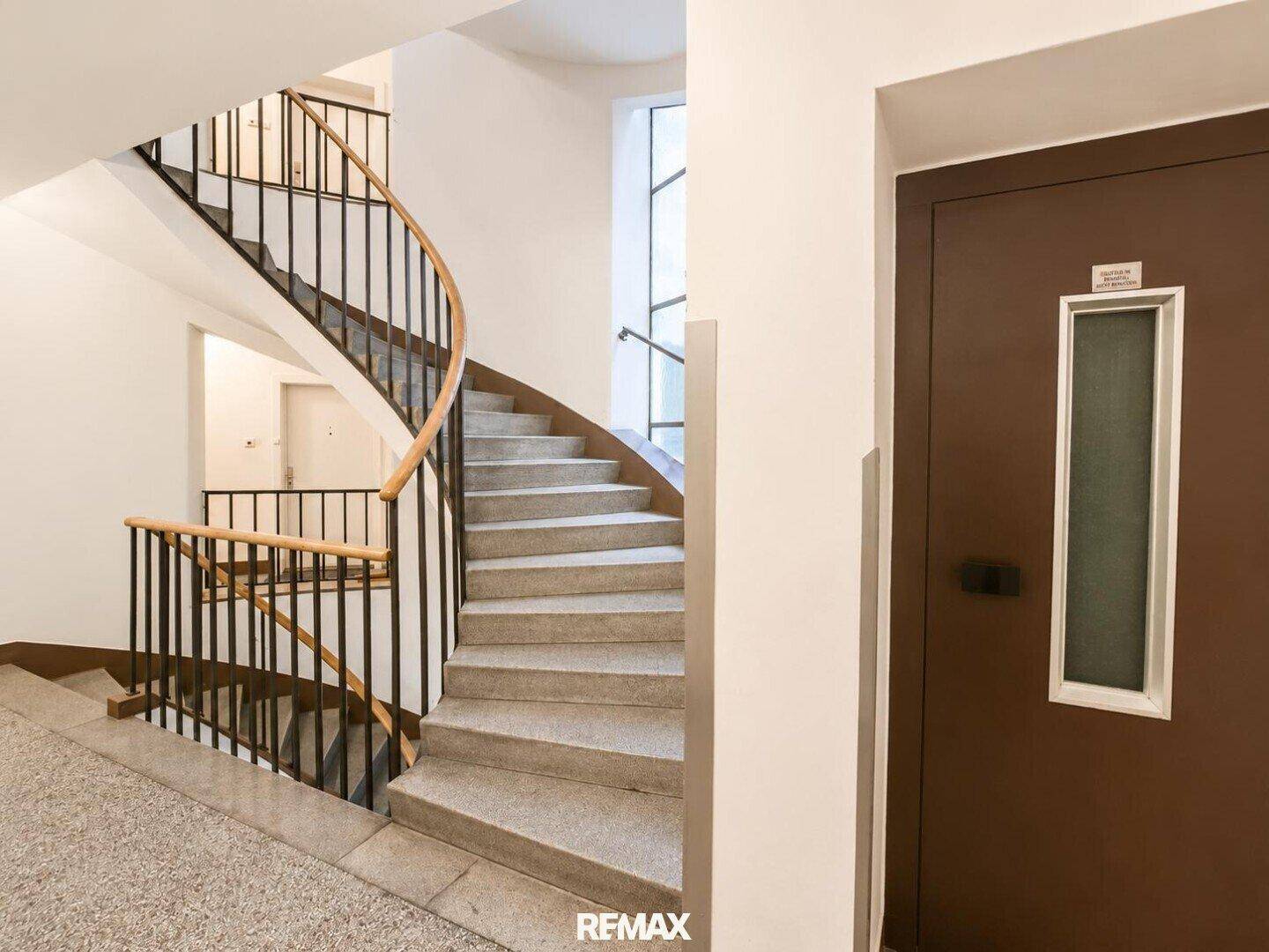 Elegantes Treppenhaus mit geschwungener Holztreppe und Zugang zum Aufzug.