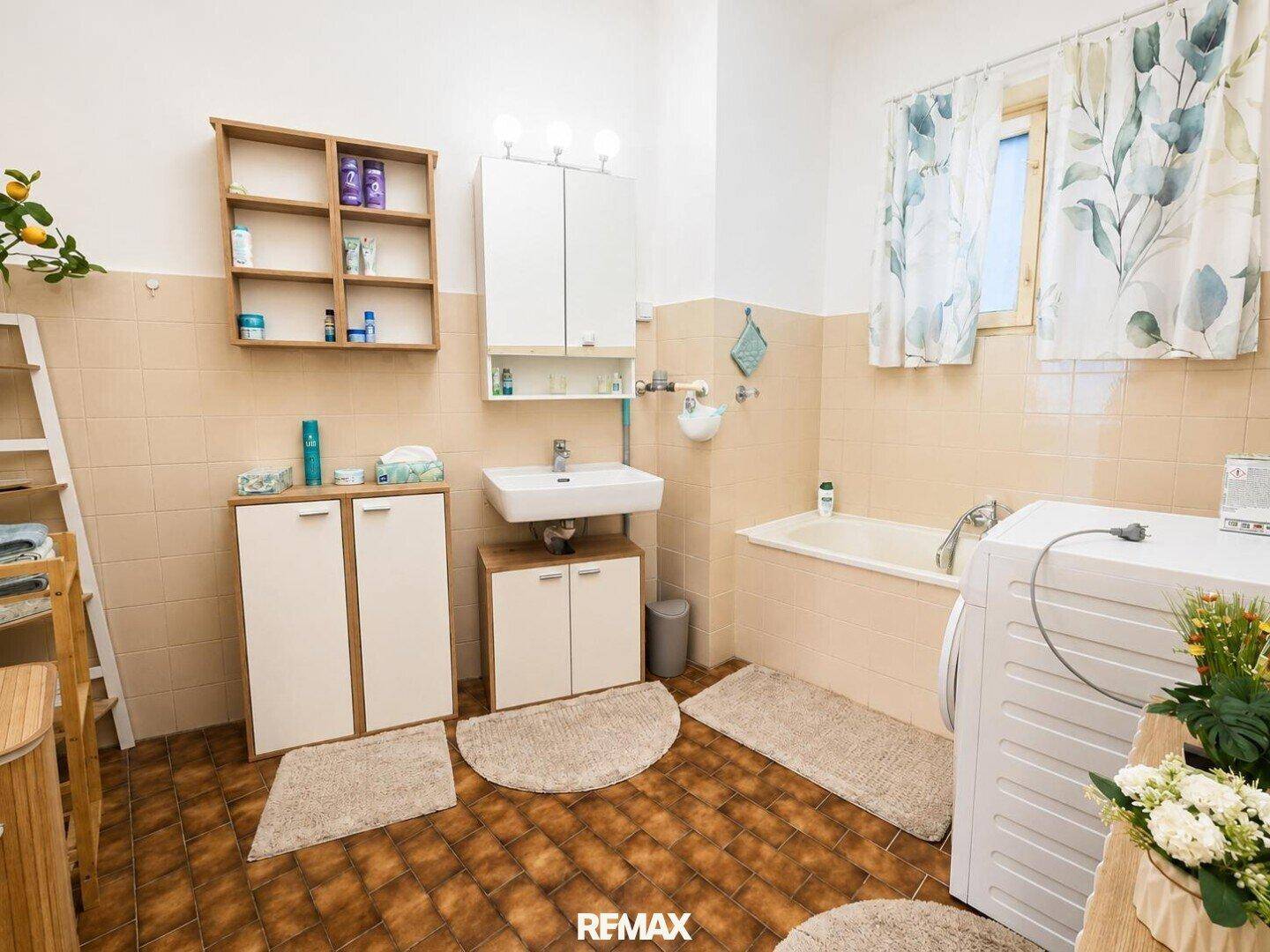 Helles Badezimmer mit Badewanne, Waschbecken, Waschmaschine und Fenster.