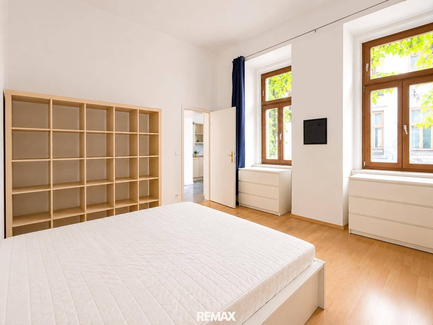 Geräumiges Schlafzimmer mit Holzboden, weißen Möbeln und zwei großen Fenstern.