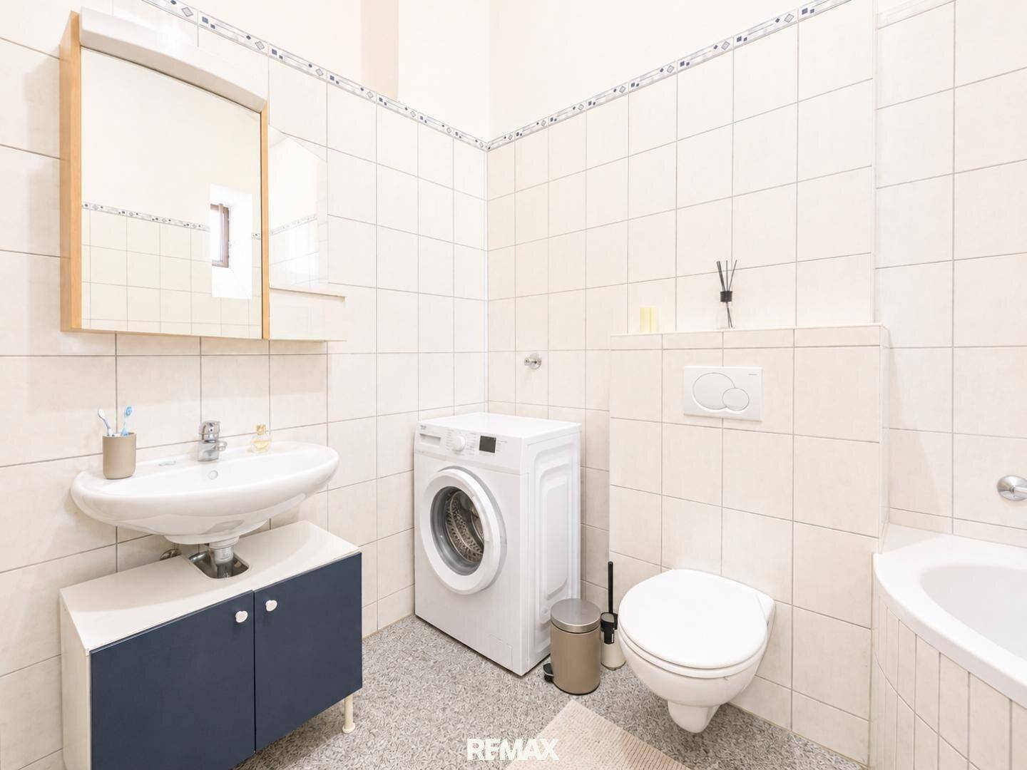 Helles Badezimmer mit Waschbecken, Spiegelschrank, Toilette und Waschmaschine.