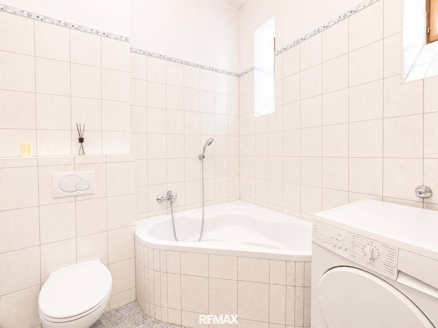 Gefliestes Badezimmer mit Eckbadewanne, Toilette und Waschmaschine.