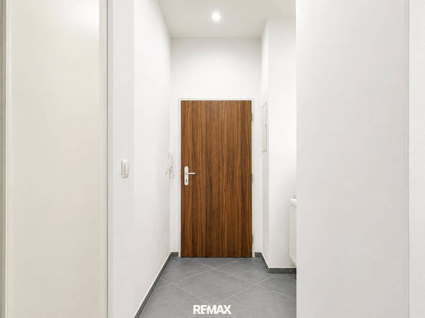 Heller Flur mit Fliesenboden und einer modernen Holztür, die zum Eingangsbereich führt.