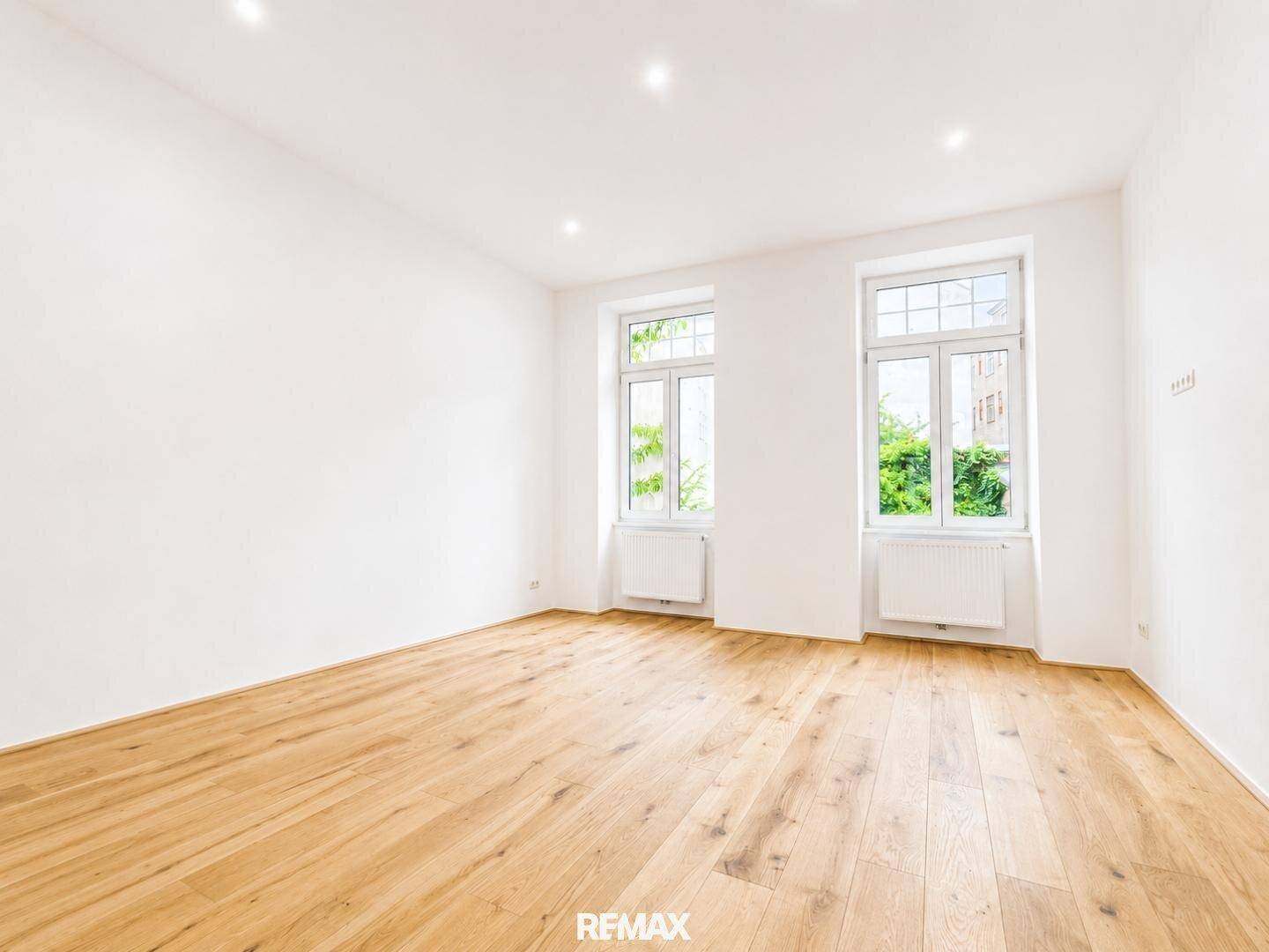 Geräumiger, heller Raum mit Holzboden und großen Fenstern, die viel Tageslicht hereinlassen.