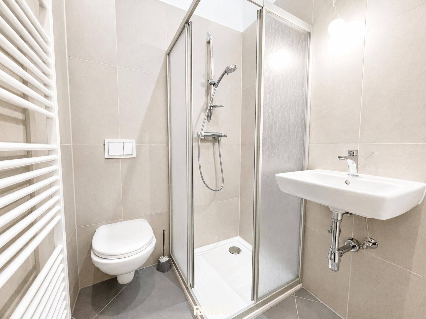 Modernes Badezimmer mit Dusche, WC, Waschbecken und beheiztem Handtuchhalter, hell gefliest.